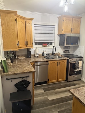 A compact kitchen with wooden cabinets, a stainless steel dishwasher, a stove, and a microwave.