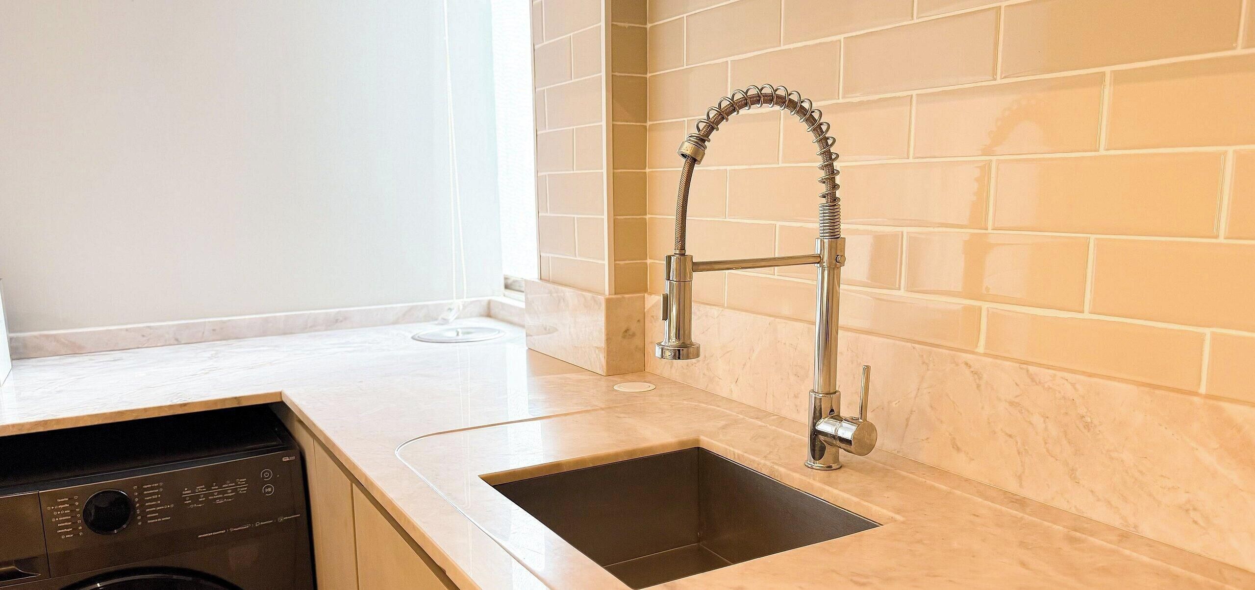 Una cocina con un lavamanos de acero inoxidable, lavavajillas y salpicadero de azulejos.