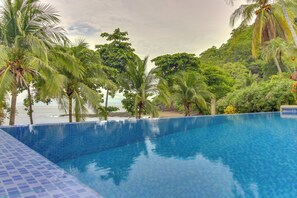 A clear blue pool with a tiled edge, surrounded by lush greenery and palm trees, overlooking a beach. - 2-Unit Bundle: Bahia Pez Vela Resort Villas (Playa Ocotal)