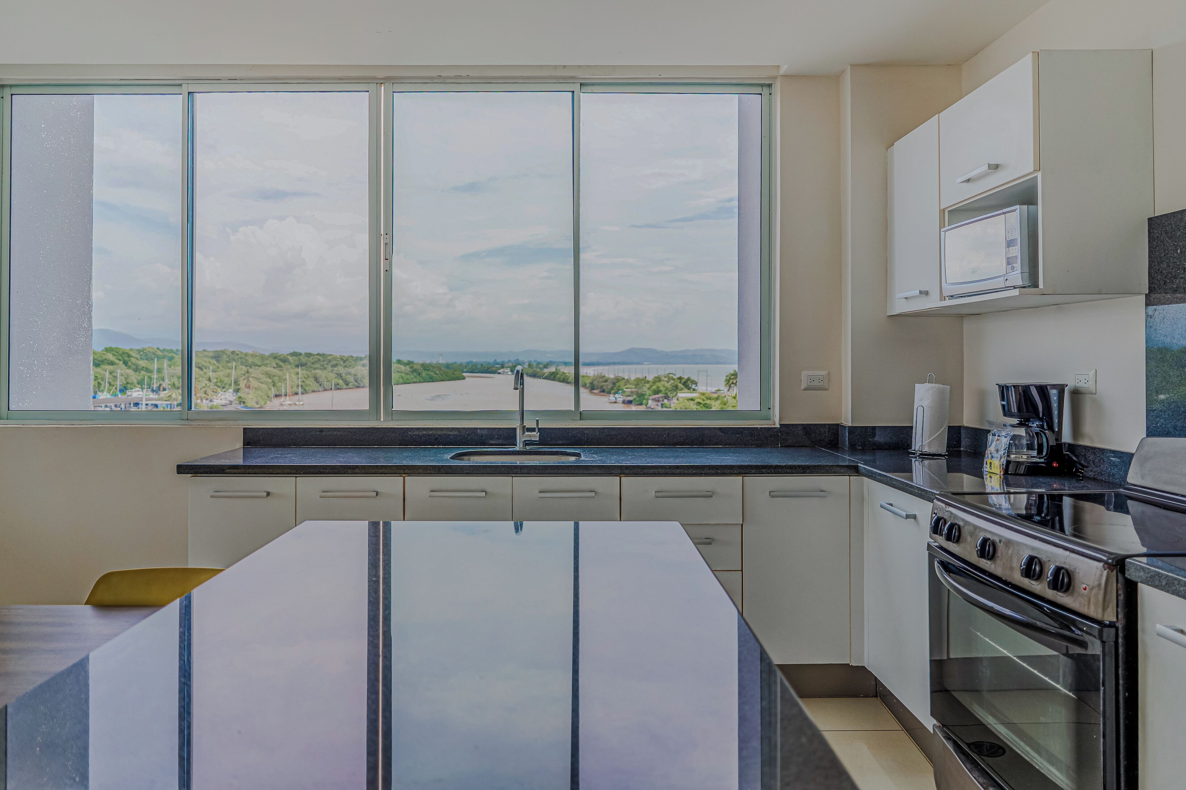 A kitchen with a large window, a stove, and cabinets.