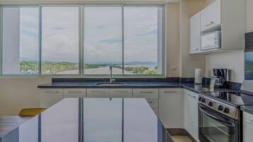 A kitchen with a large window, a stove, and cabinets.
