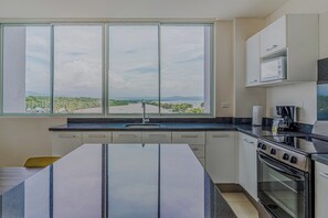 A kitchen with a large window, a stove, and cabinets.