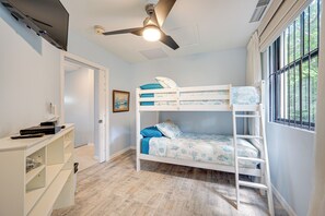 A bunk bed room with a ceiling fan, a painting on the wall, and a window with blinds.