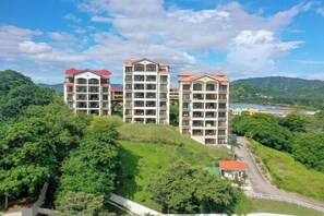 Een hotel met meerdere verdiepingen en balkons, gelegen tegen een achtergrond van weelderige begroeiing en een heldere lucht.