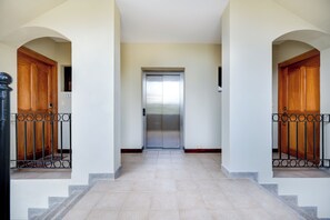 A hallway with a central elevator, flanked by wooden doors and metal railings.