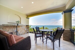 A covered patio with a stone wall, a table with chairs, and a view of the ocean.