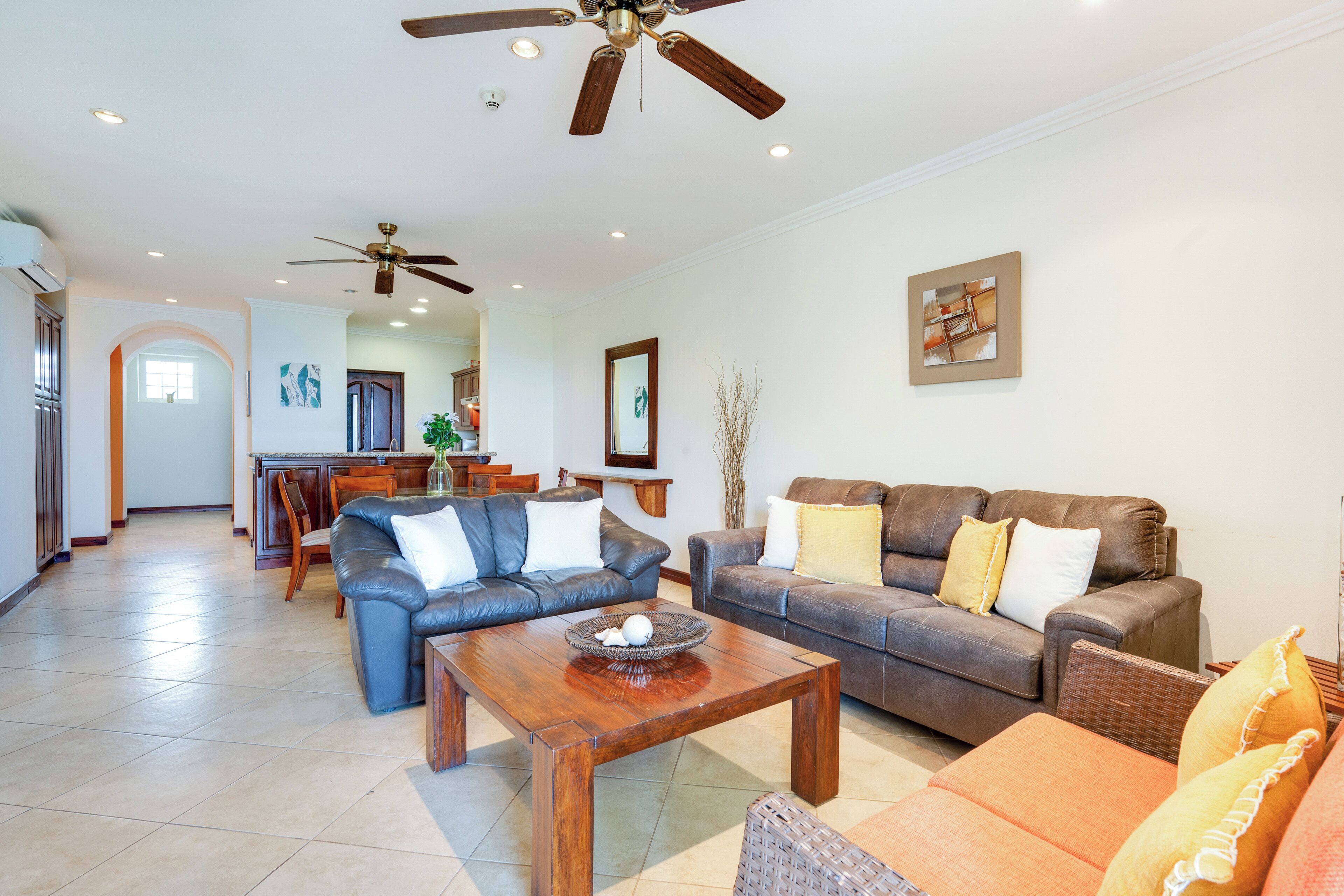 A spacious living area with a ceiling fan, a dining area with a kitchen in the background, and a large window providing natural light.