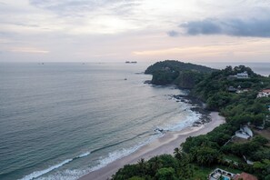 A coastal landscape with a beach, rocky shoreline, and a hill with buildings.