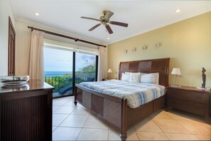 A bedroom with a large bed, a nightstand, a dresser, a ceiling fan, and a view of the outdoors.