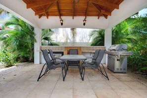 Een terras buiten met een tafel, stoelen, een barbecue en weelderige begroeiing.