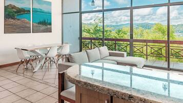 A modern room with a large window, a dining area, and a seating area with a view of the landscape.