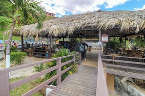 A covered outdoor seating area with wooden tables and chairs, a thatched roof, and a wooden walkway leading to it. - Playa del Coco 3BR: Ocean Views & Pools! (Playa Hermosa)