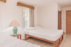 A room with two wooden beds, a bedside table with a lamp, a window with curtains, and a wooden door. - Playa del Coco 3BR: Ocean Views & Pools! (Playa Hermosa)
