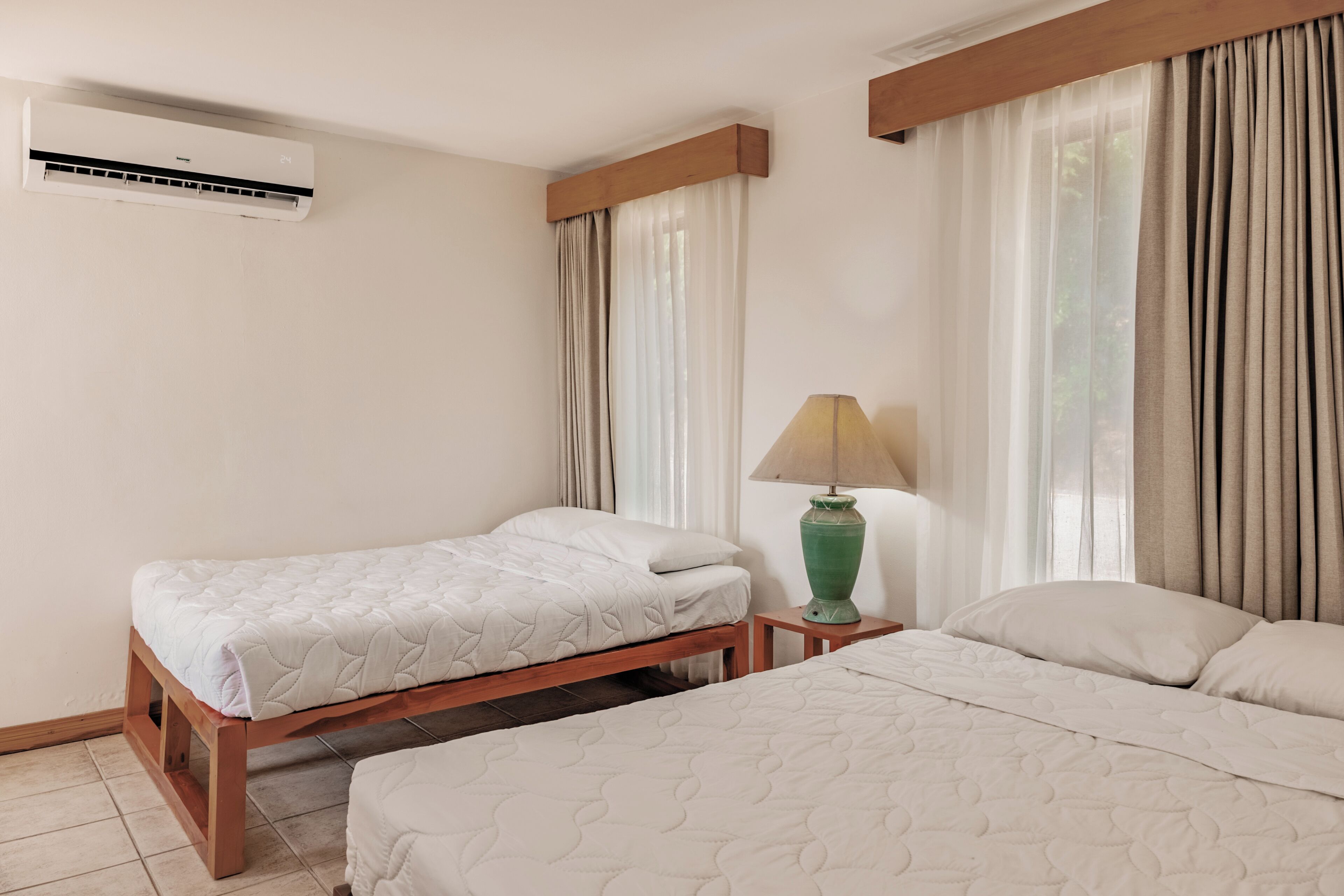 A hotel room with two beds, a nightstand, a lamp, and an air conditioning unit.