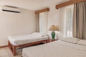 A hotel room with two beds, a nightstand, a lamp, and an air conditioning unit.