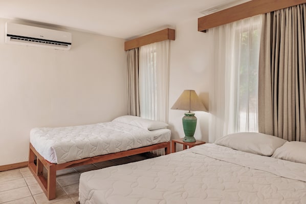 A hotel room with two beds, a nightstand, a lamp, and an air conditioning unit.