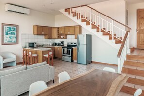 A modern kitchen with wooden cabinets, a dining area with a wooden table, and a staircase with wooden railings.