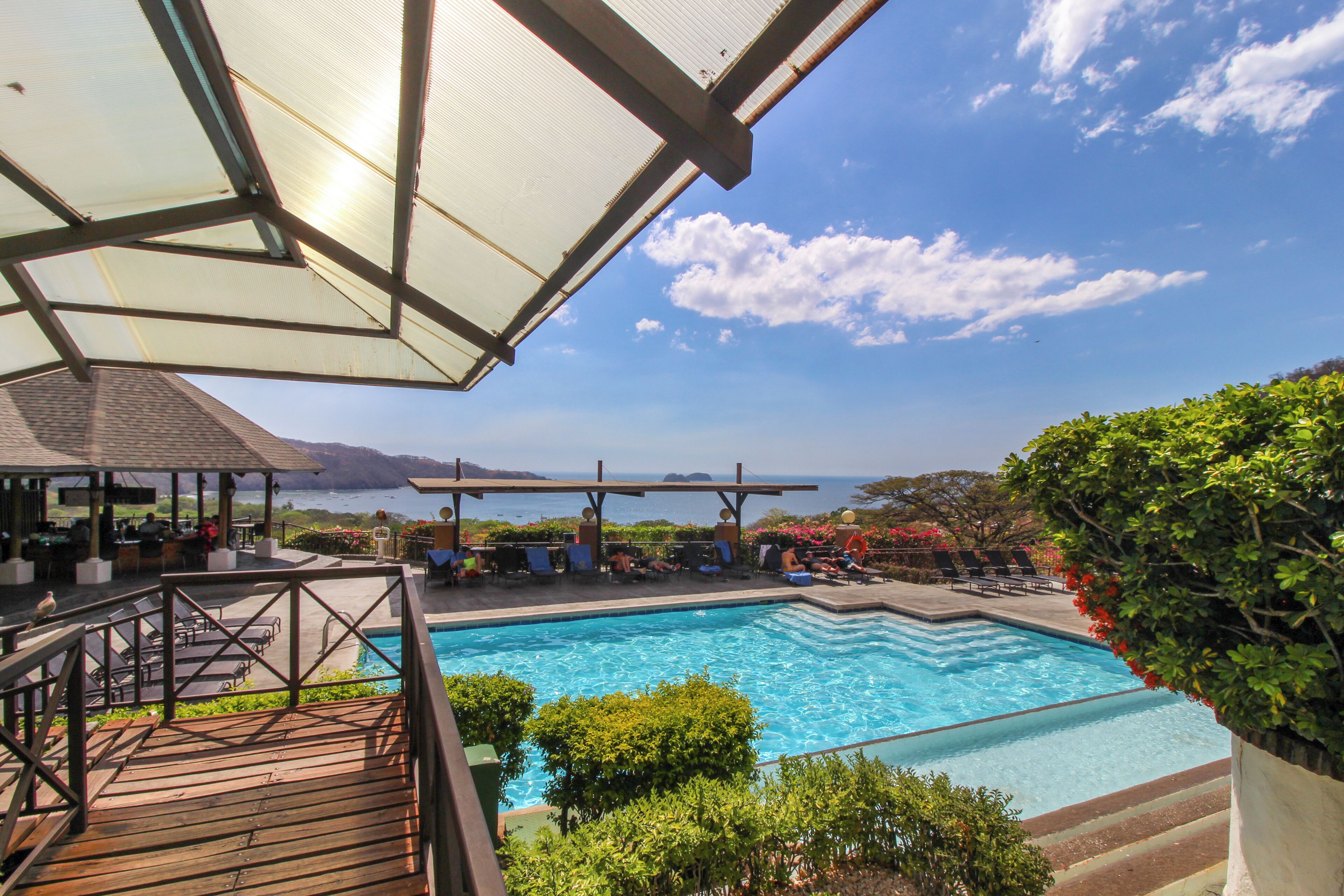 Une piscine avec vue sur la mer, entourée de chaises longues et d’une terrasse en bois.