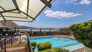 Une piscine avec vue sur la mer, entourée de chaises longues et d’une terrasse en bois.