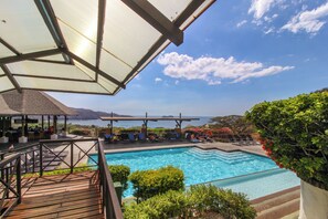 A swimming pool with a view of the sea, surrounded by lounge chairs and a wooden deck.