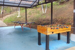 An outdoor area with a foosball table and a ping pong table under a covered structure.