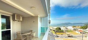 Varanda com mesa e cadeiras, com vista para uma vila costeira e montanhas.
