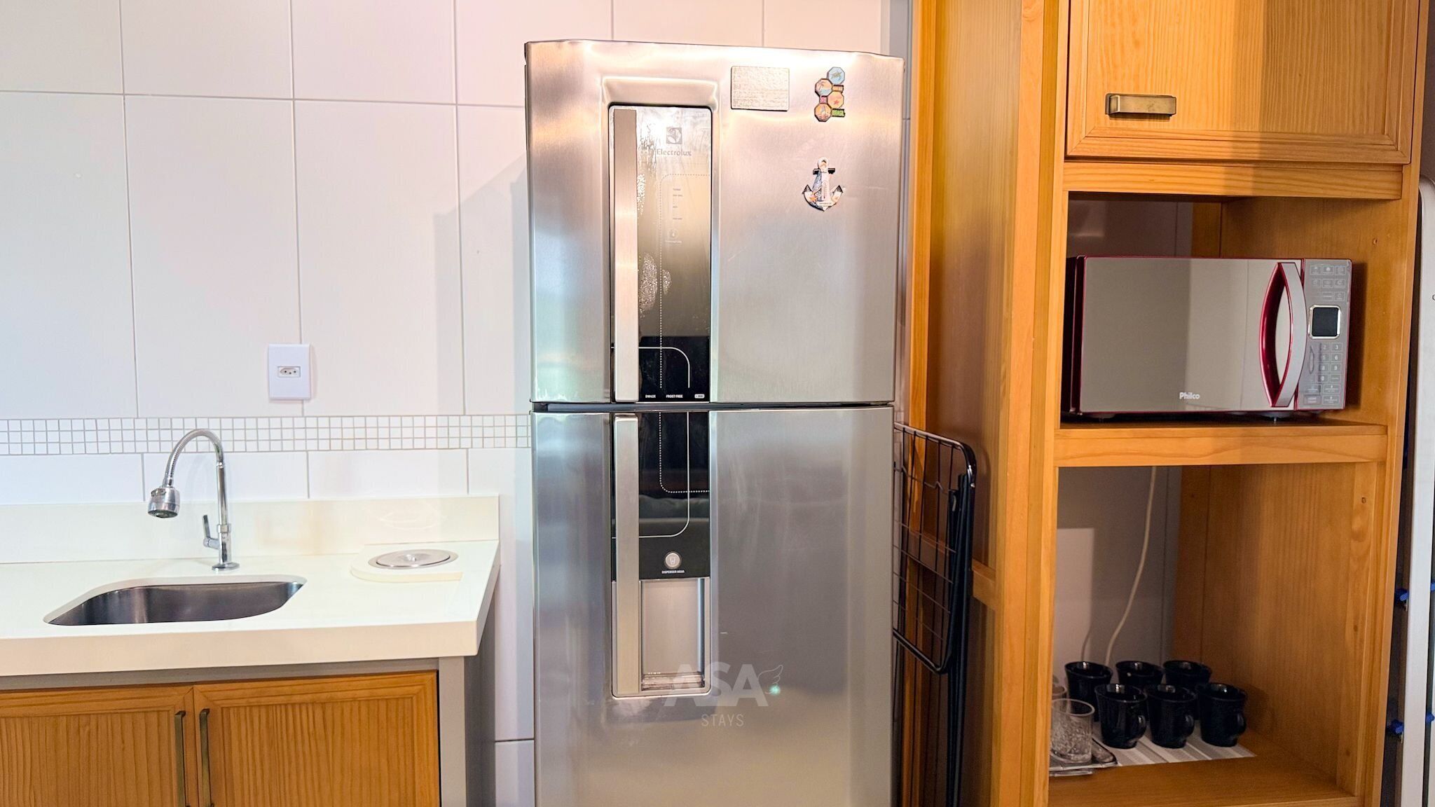 Ein Edelstahl-Kühlschrank mit Wasserspender und Eiswürfelbereiter, darüber eine Mikrowelle und darunter ein Holzschrank mit Ablagefläche.