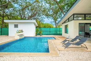 A swimming pool with lounge chairs and a small shed, surrounded by a green fence and trees. - Brasilito Family Villa: Pool, Walk to Beach (Brasilito)