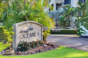 Schild für 'CONDOMINIOS OCEANICA' mit steinernen Fundament, umgeben von tropischen Pflanzen und einer gepflasterten Fläche.