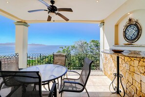 A covered patio with a table and chairs, a ceiling fan, a decorative wall piece, and a view of the sea. - Best Flamingo Beach View! Pool, Balcony (Flamingo Beach)