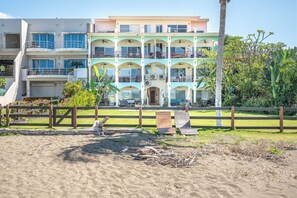 Een hotel met meerdere verdiepingen, voorzien van balkons, een zwembad en een zandstrand.