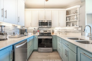 Une cuisine moderne dotée d’appareils électroménagers en acier inoxydable, de meubles de couleur bleu clair et d’un pare-feu en marbre.