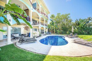 A multi-story building with a swimming pool, outdoor seating, and lush greenery.