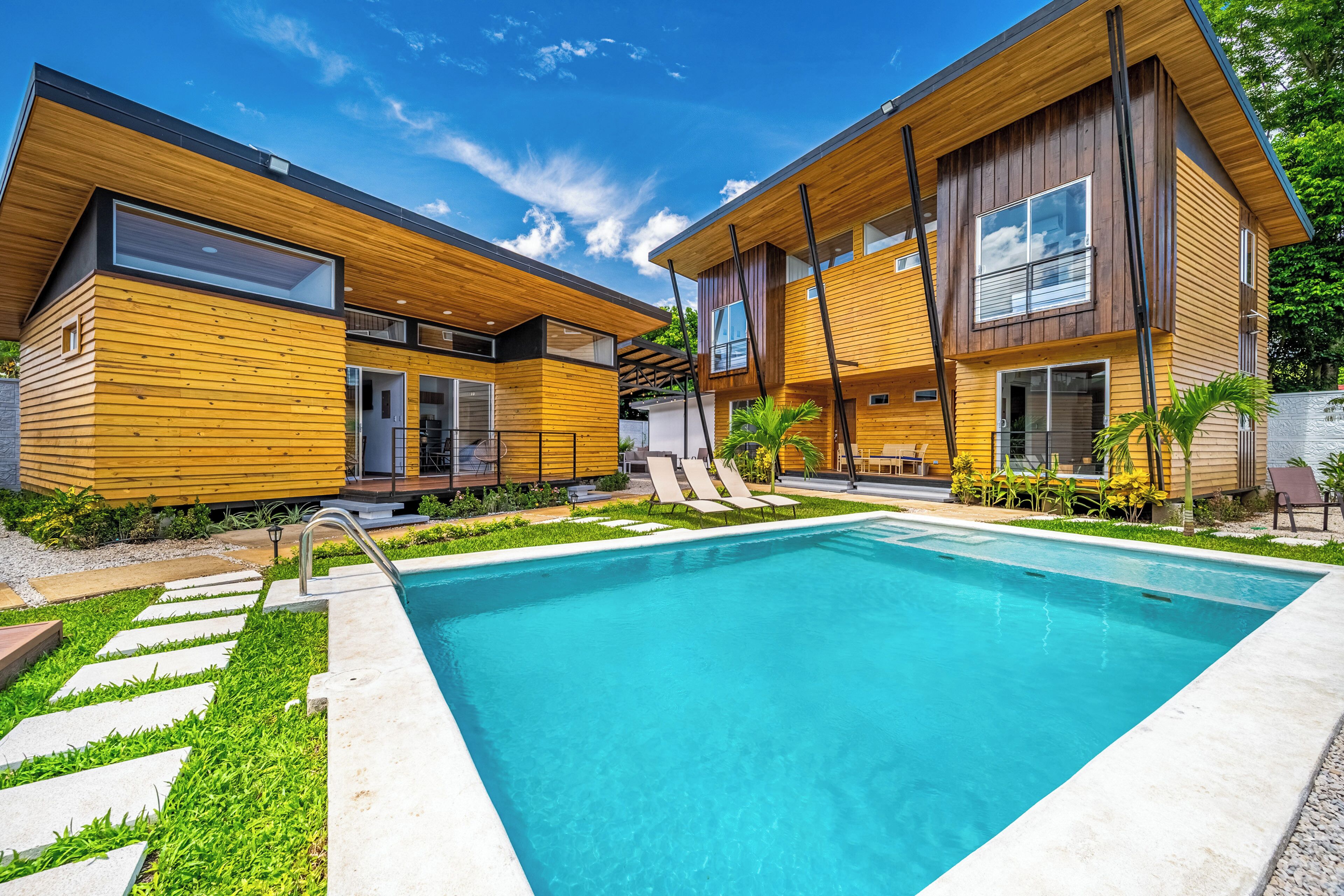 A modern two-story house with a swimming pool, wooden exterior, and a well-maintained garden.