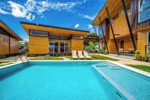 A modern poolside area with a clear blue pool, wooden exterior buildings, and a well-maintained garden. - Walk to Del Coco Beach & Restaurants: 2 Condos! (Playas del Coco)
