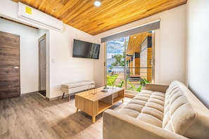 A modern living room with a wooden ceiling, a flat-screen TV mounted on the wall, a sofa, a coffee table, and a sliding glass door leading to an outdoor area. - Walk to Del Coco Beach & Restaurants: 2 Condos! (Playas del Coco)