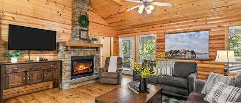A log cabin interior with a fireplace, television, sofa, and a ceiling fan.