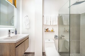 A modern bathroom with a glass shower enclosure, a toilet, and a sink with a wooden vanity. - 'Veranera' Condo w/ Pool Access, 1/2 Mi to Beach! (Playas del Coco)