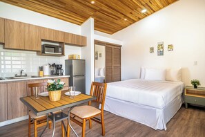 Ein kompaktes Hotelzimmer mit Küchenzeile, einem Bett, einer Essecke und einem kleinen Nachttisch.
