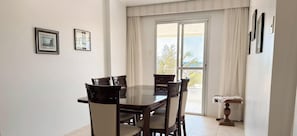 A dining area with a glass-top table and four chairs, a sliding glass door to a balcony, and two framed pictures on the wall. - ASA Apto Frente Mar Barra Norte BC (Balneário Camboriú)