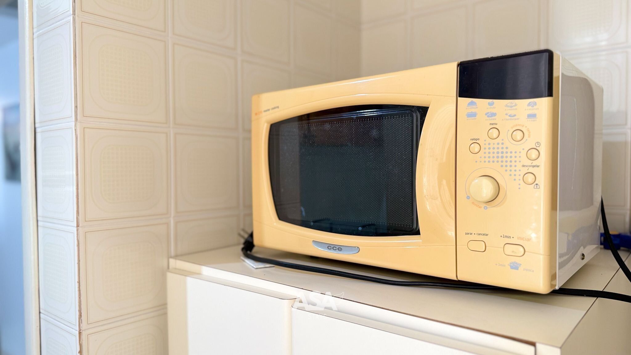 A microwave oven on a white cabinet with a tiled wall background.
