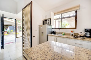 A modern kitchen with a granite countertop, stainless steel appliances, and a window with a view of the outdoors. - Step-Free Studio w/ Pool Access, Walk to Beach! (Playas del Coco)