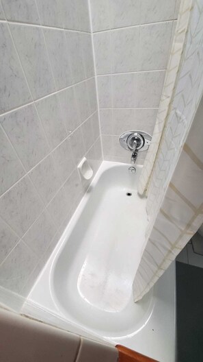 Une baignoire avec un drain, un rideau de douche et un mur carrelé.