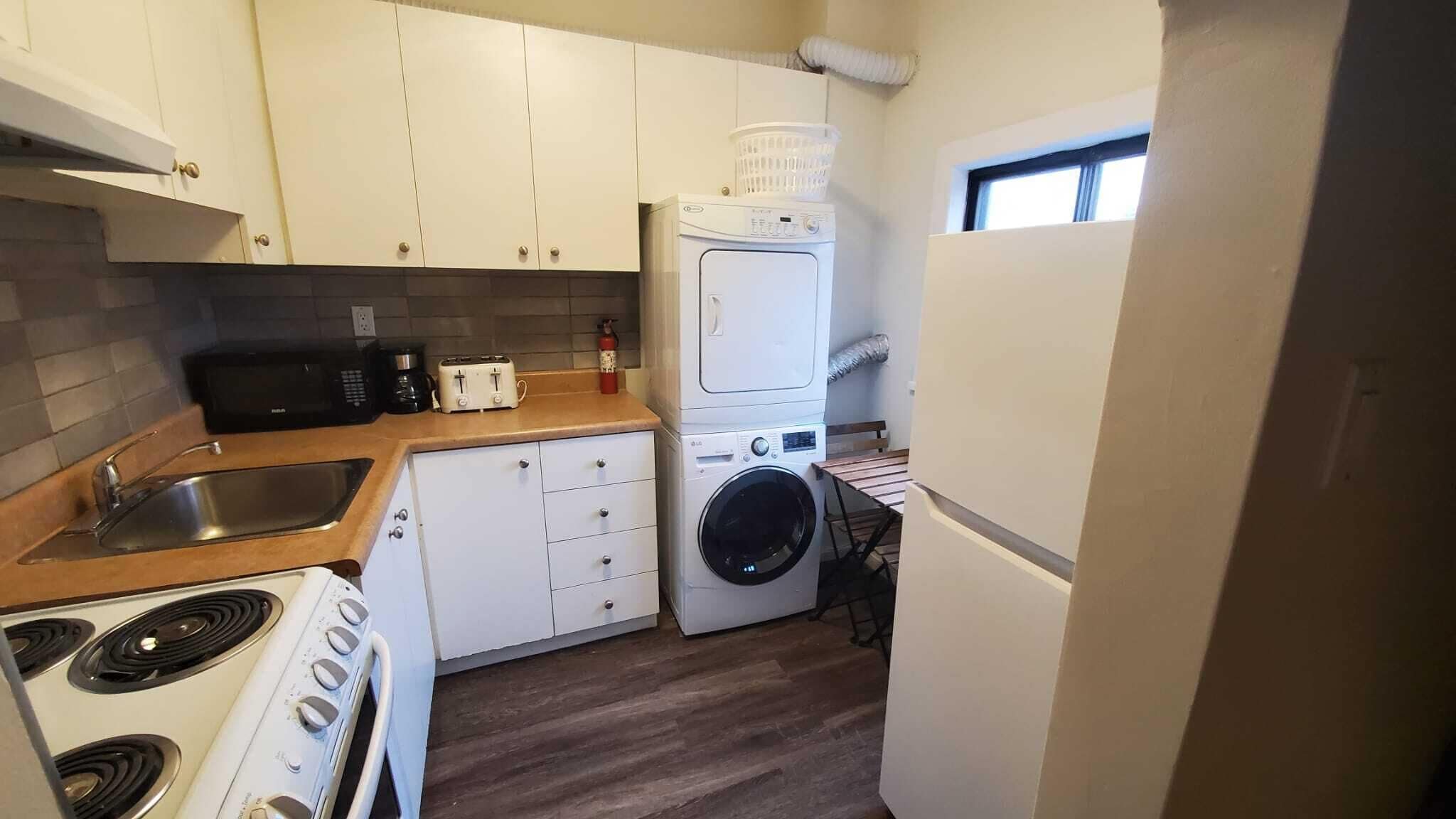 Ett kompakt kök med spis, diskho, mikrovågsugn, brödrost och en kombinerad tvätt- och torkmaskin.