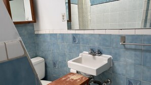 Casa de banho com uma pia branca, azulejos azuis, um banco de madeira e um espelho.