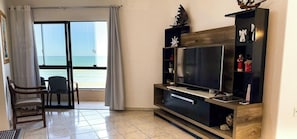 Ein Wohnzimmer mit Fernseher, einer Holz-Unterhaltungseinrichtung und Meerblick durch eine Glastür.