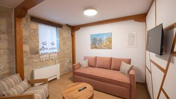 Ein gemütliches Wohnzimmer mit einer Couch, einem Holztisch und einem an der Wand befestigten Fernseher.