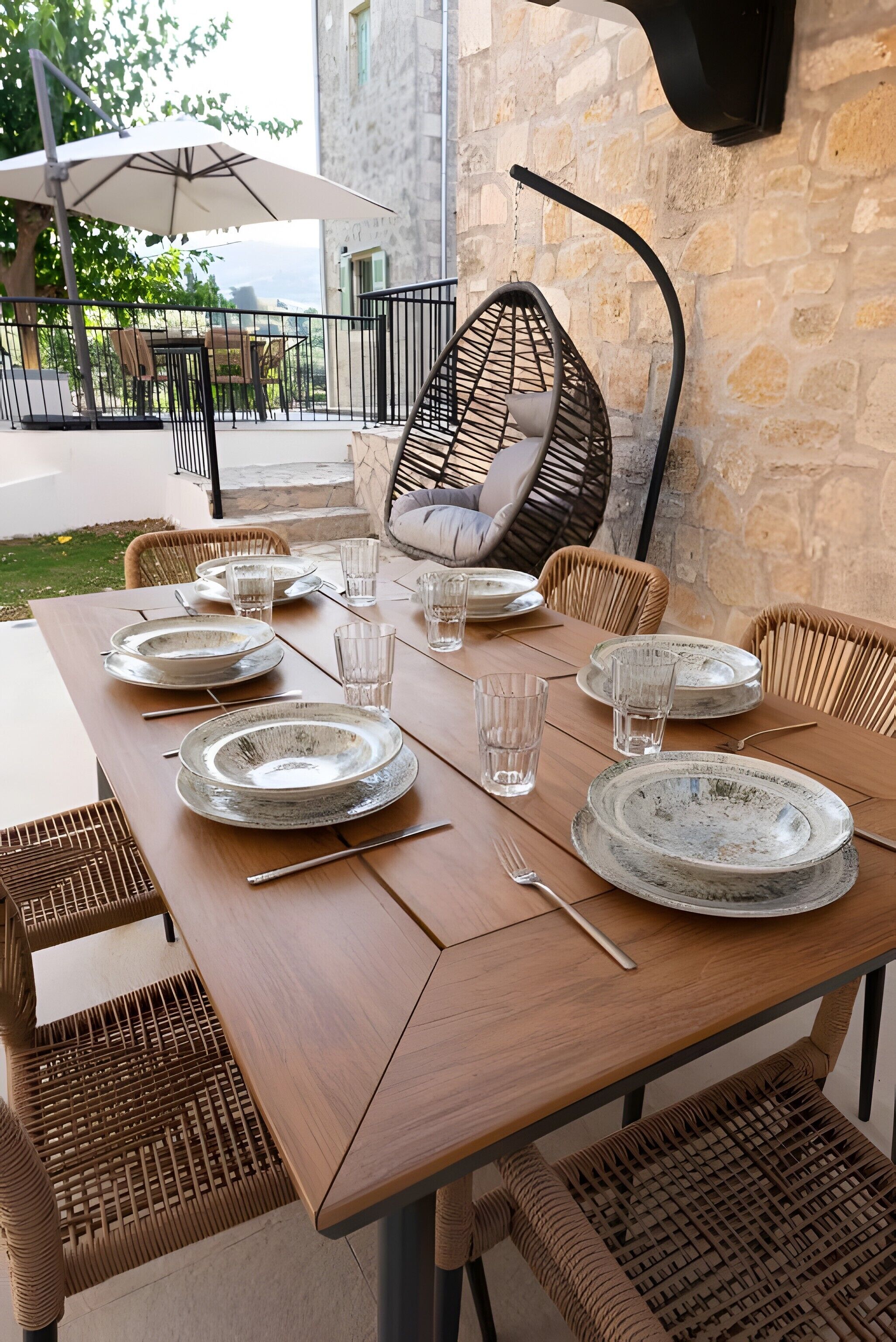 A wooden dining table set with plates, glasses, and cutlery, surrounded by wicker chairs.