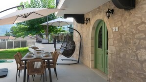 Une terrasse extérieure avec une table dressée pour le repas, un fauteuil suspendu et une porte verte.