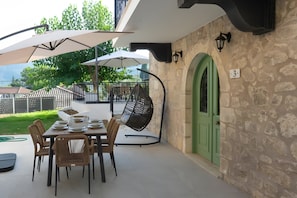 An outdoor patio with a table set for dining, a hanging chair, and a green door. - Apartment 'Dervisia Stone Houses 3' with Mountain View, Wi-Fi and Air Conditioning (Lazarata)